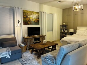 A modern living room with a sofa, a television, a coffee table, and a painting on the wall. - Private Casita w/ New Full Kitchen, Private Pool, Gated Community (Goodyear)