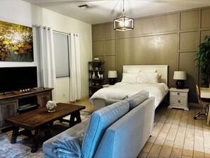 A modern bedroom with a bed, bedside tables, a TV, and a sofa.