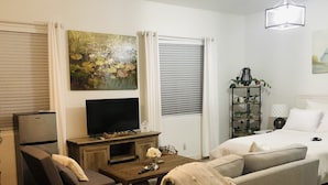 A modern living room with a sofa, a television, a coffee table, and a bookshelf. - Private Casita w/ New Full Kitchen, Private Pool, Gated Community (Goodyear)