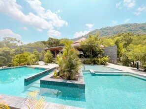 Un área de piscina con agua azul cristalina, rodeada de exuberante vegetación y montañas al fondo.