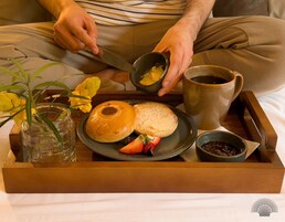 Uma bandeja com um bagel, morangos, café e um pequeno vaso com flores.