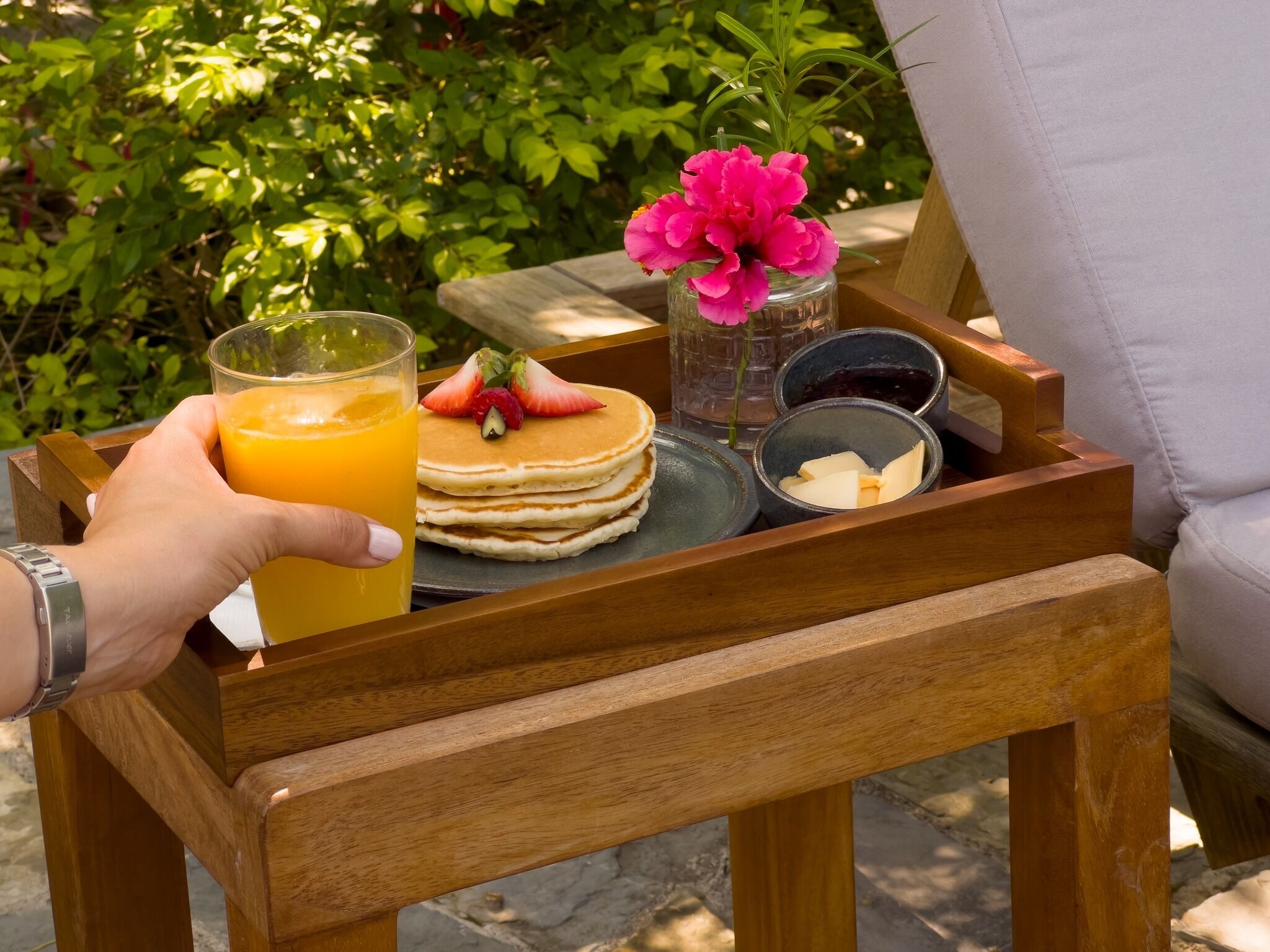Un plateau en bois avec des crêpes, un verre de jus d’orange, une fleur et un petit pot de beurre.