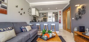 A modern living room with a grey sofa, a coffee table with a magazine, and a kitchen in the background.