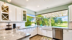 A kitchen with white cabinets, a marble countertop, and a view of a green landscape. - Mirage Oasis | 3BR Retreat with Private Pool & Jaw-Dropping Views – a Greenday property! (Rancho Mirage)