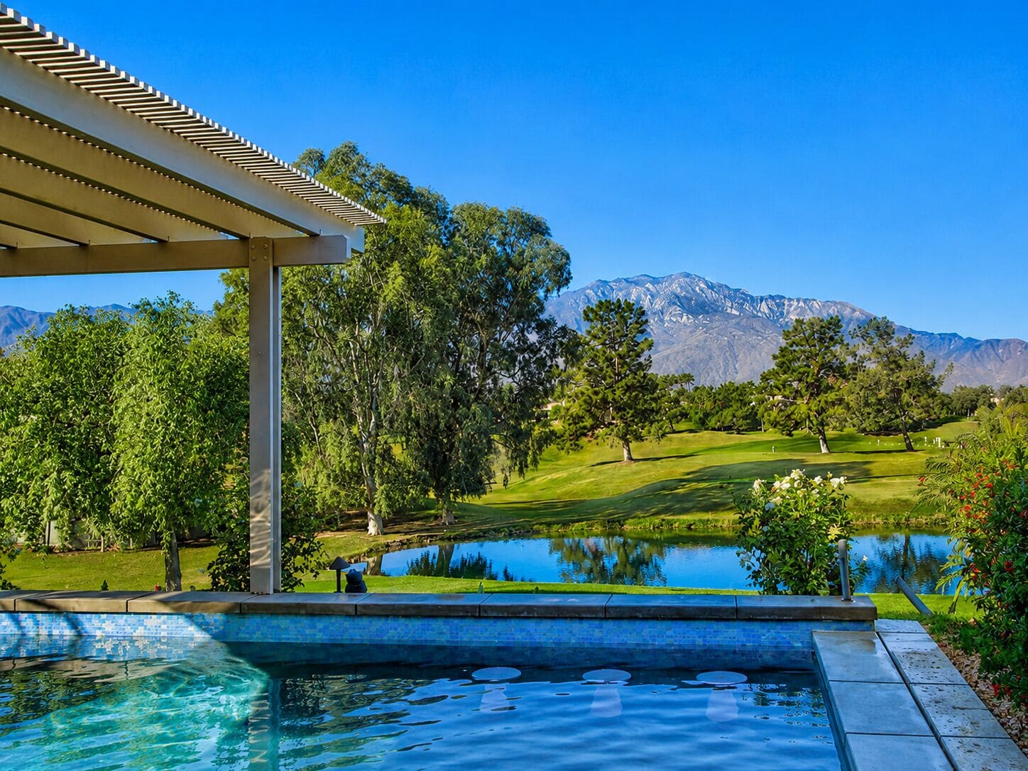 A swimming pool with a view of a golf course and mountains in the background.