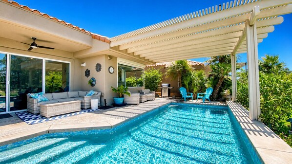 A swimming pool with a pergola, outdoor seating, and a barbecue area.