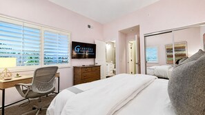 A hotel room with a bed, a desk, a chair, a dresser, a television, and a window with blinds.