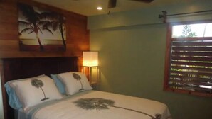 A bedroom with a bed, a ceiling fan, a wall-mounted lamp, and a window with blinds. - May Rose Cottage lower level (Captain Cook)