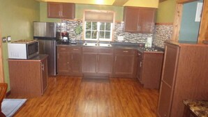 A kitchen with wooden cabinets, a stainless steel refrigerator, a microwave, and a sink. - May Rose Cottage lower level (Captain Cook)