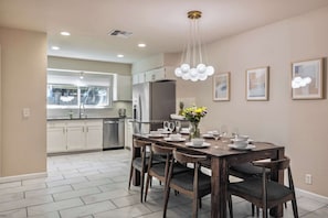 A modern kitchen with white cabinets, a stainless steel refrigerator, and a dining area with a wooden table and chairs.