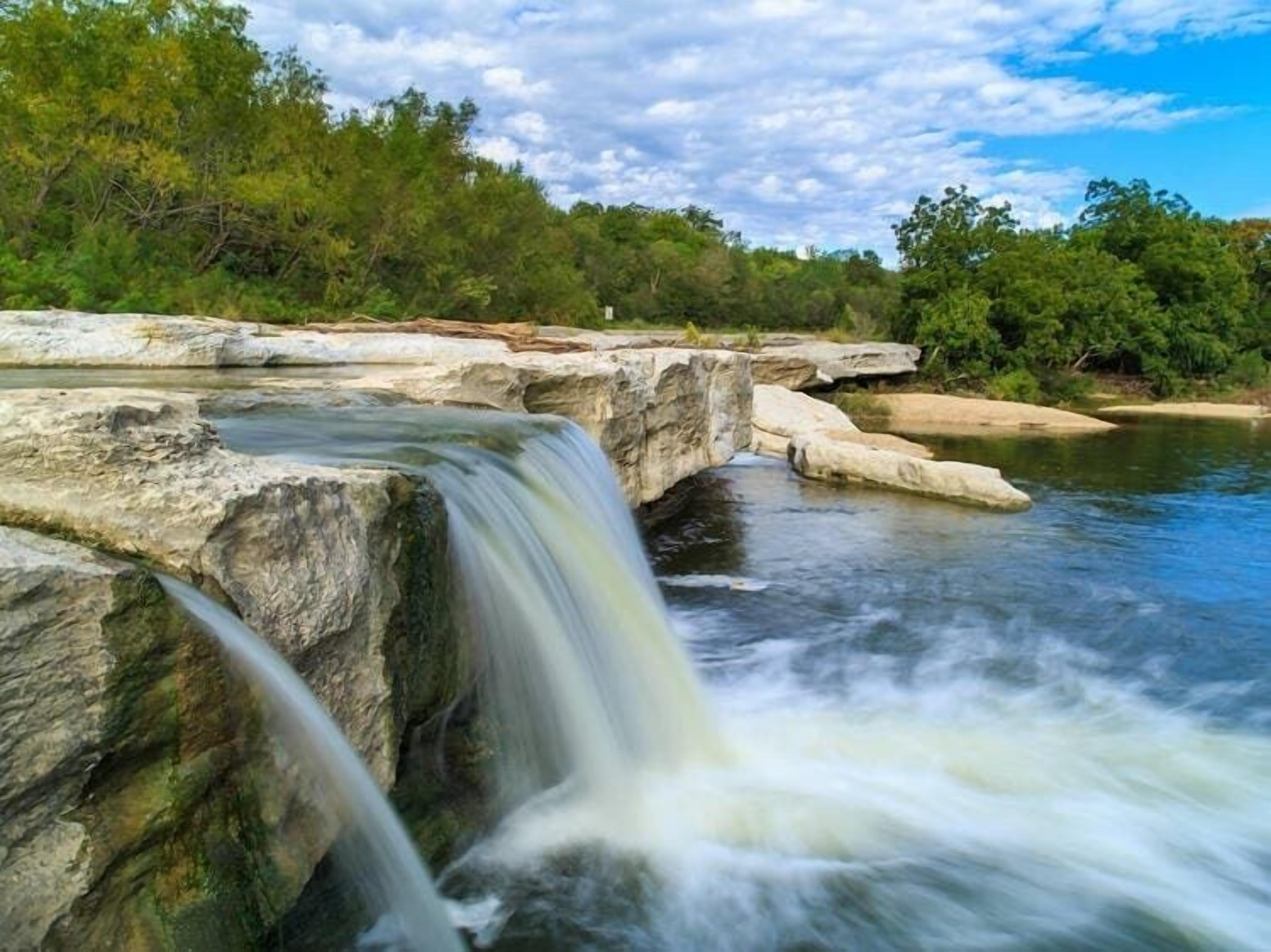 A waterfall cascading over rocky terrain with a forested backdrop.