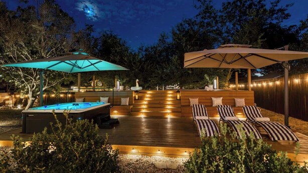Een houten terras met een jacuzzi, lounge fauteuils en parasols.