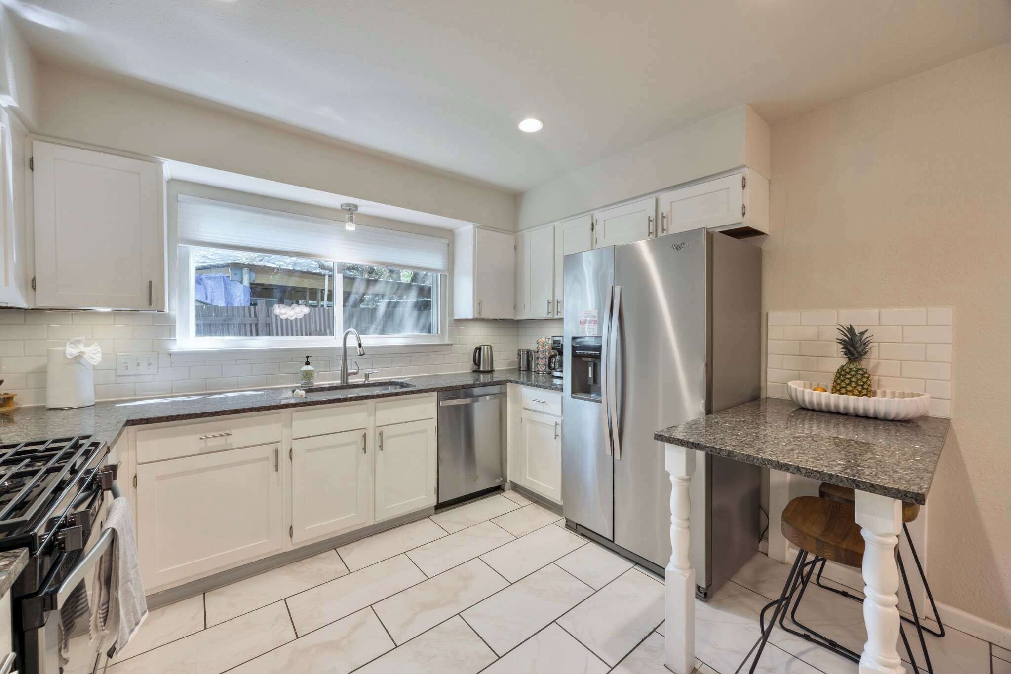 A modern kitchen with white cabinets, stainless steel appliances, a granite countertop, and a window with a view.