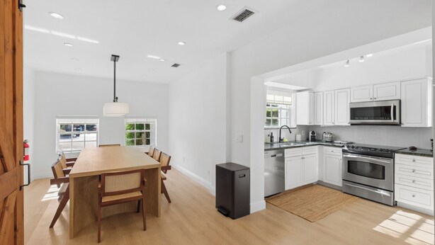 Une cuisine moderne avec des meubles blancs, des appareils en acier inoxydable et une table à manger en bois.