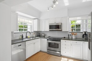 Une cuisine moderne avec des meubles blancs, des appareils électroménagers en acier inoxydable et un plancher en bois.