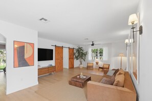 Un vaste espace de vie comprenant un grand téléviseur à écran plat, des portes coulissantes en bois, une plante en pot, un canapé et une table basse.