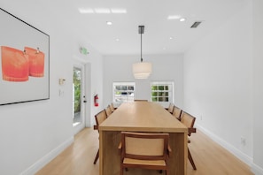 A spacious dining area with a long wooden table, multiple chairs, a pendant light, and a fire extinguisher on the wall.
