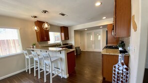 Una cocina amplia con una isla central, taburetes blancos de bar, armarios de madera y una lámpara colgante moderna.