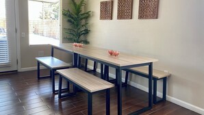 Un comedor con mesa de madera y bancos, una planta en maceta y decoración en la pared.
