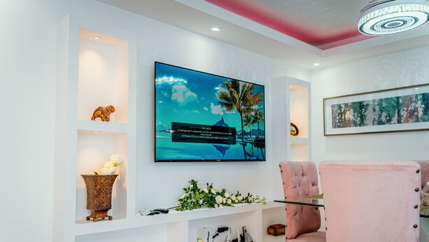 Una sala moderna con un televisor de pantalla plana montado en la pared, un sillón tapizado en rosa y un mueble bajo blanco con objetos decorativos.