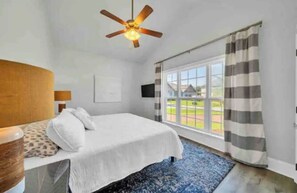 A bedroom with a bed, a ceiling fan, a window with curtains, and a view of a house. - Sea Pearl: Newly Renovated, Family Getaway on 30A! (Santa Rosa Beach)