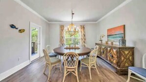 Une salle à manger avec une table ronde, quatre chaises, un lustre, un buffet en bois et un tableau accroché au mur.