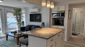 Une cuisine moderne dotée d’un plan de travail en granit, de meubles blancs et d’un four à micro-ondes encastré. On y trouve également un coin repas avec une table et des chaises en verre, ainsi qu’une grande fenêtre donnant sur un plan d’eau.