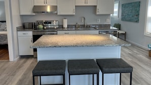 Une cuisine moderne avec des meubles blancs, des plans de travail en granit, des appareils électroménagers en acier inoxydable et un îlot central doté de tabourets de bar.