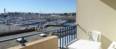 A balcony with a view of a marina filled with boats, a table, and two chairs.
