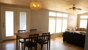 A spacious living area with a wooden dining table and chairs, a dark sofa, and a ceiling fan. - Relaxing Rural Family Home with a great outdoor experience (Woodward)