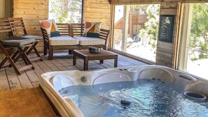 Interior de una cabaña de madera con jacuzzi, muebles de madera y grandes ventanales.