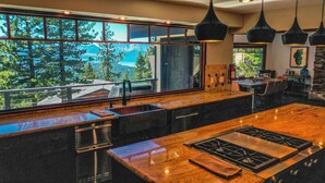 Una cocina moderna con un amplio ventanal con vistas a un área boscosa, estufa integrada e iluminación colgante.