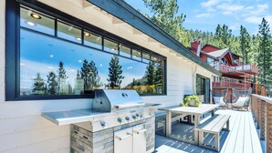 Cocina al aire libre con una parrilla y una zona de comedor en una terraza de madera.
