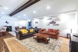 A spacious living room with a dark leather sofa, a brown leather couch, and a coffee table. There is a dining area with a table and chairs, and a bookshelf. - "Stadium Oasis" - A quick walk to the stadiums! (Arlington)