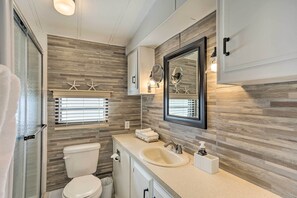 A modern bathroom with a wooden wall backsplash, a large mirror, a toilet, and a sink with a soap dispenser. - Jensen Beach Home w/ Private Beach Access! (Jensen Beach)