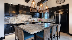 A kitchen with dark wood cabinets, a marble countertop, a central island with bar stools, and pendant lighting. - Ocean View Hacienda de Mita Penthouse, Premier Golf  (Punta de Mita)