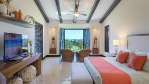 A hotel room with a bed, a TV, a desk, and a view of the ocean.