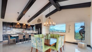 A modern kitchen with dark wooden beams, pendant lights, and a dining area with a wooden table and green upholstered chairs. - Ocean View Hacienda de Mita Penthouse, Premier Golf  (Punta de Mita)