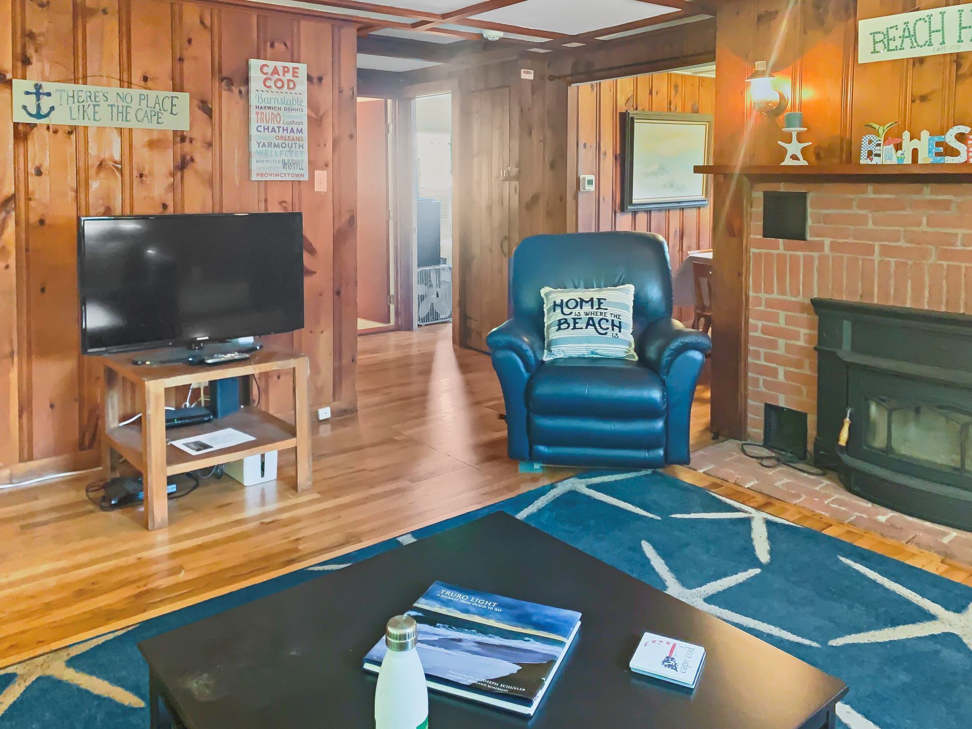 Een gezellige kamer met een televisie op een houten standaard, een blauwe leren fauteuil met een kussen, een open haard en een blauw vloerkleed.