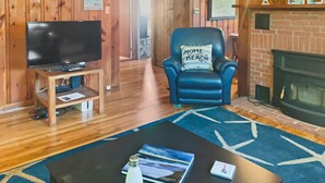 Une pièce chaleureuse avec un téléviseur posé sur un meuble en bois, un fauteuil en cuir bleu avec un coussin, une cheminée et un tapis bleu.
