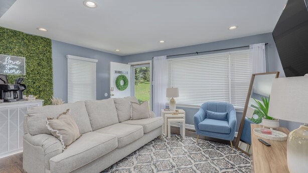 Un salon moderne avec un canapé beige, un fauteuil bleu, un tapis à motifs et un mur vert.