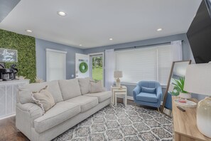 A modern living room with a beige sofa, a blue armchair, a patterned rug, and a green wall. - Cozy Downtown Bristol Cottage - 4 min to CASINO (Bristol)