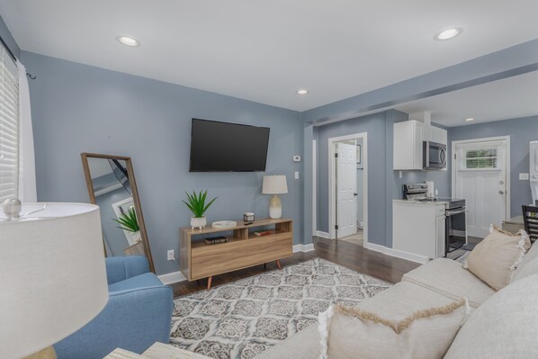A living room with a blue sofa, a wooden entertainment unit, a flat-screen TV, and a patterned rug. - Cozy Downtown Bristol Cottage - 4 min to CASINO (Bristol)