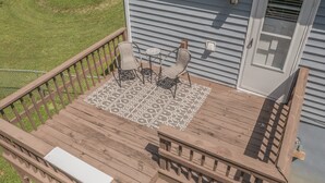 Une terrasse en bois agrémentée d’un tapis à motifs, de deux chaises et d’une petite table.