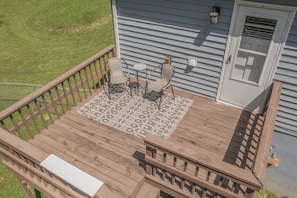 Una terraza de madera con alfombra estampada, dos sillas y una mesita.