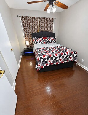 Une chambre à coucher avec un lit, un ventilateur de plafond, une table de chevet et un rideau à motifs.