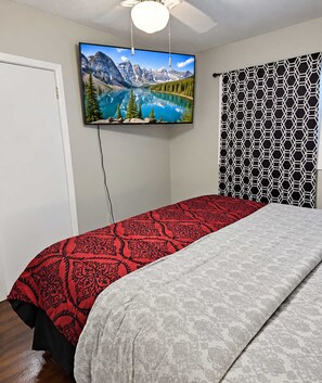 Ein Schlafzimmer mit einem Bett, einem an der Wand montierten Fernseher und einem gemusterten Vorhang.