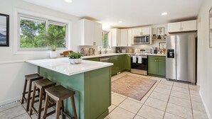 A modern kitchen with green cabinets, a white island, and stainless steel appliances. - Modern Huge Family Getaway | Fire Pit | 5BD/3BA (Arvada)