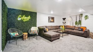 A modern living room with a green wall, a neon sign, a brown leather sofa, and a round wooden coffee table. - Modern Huge Family Getaway | Fire Pit | 5BD/3BA (Arvada)