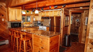 Cocina de cabaña de madera con encimera de granito, taburetes de madera, refrigerador de acero inoxidable y microondas.